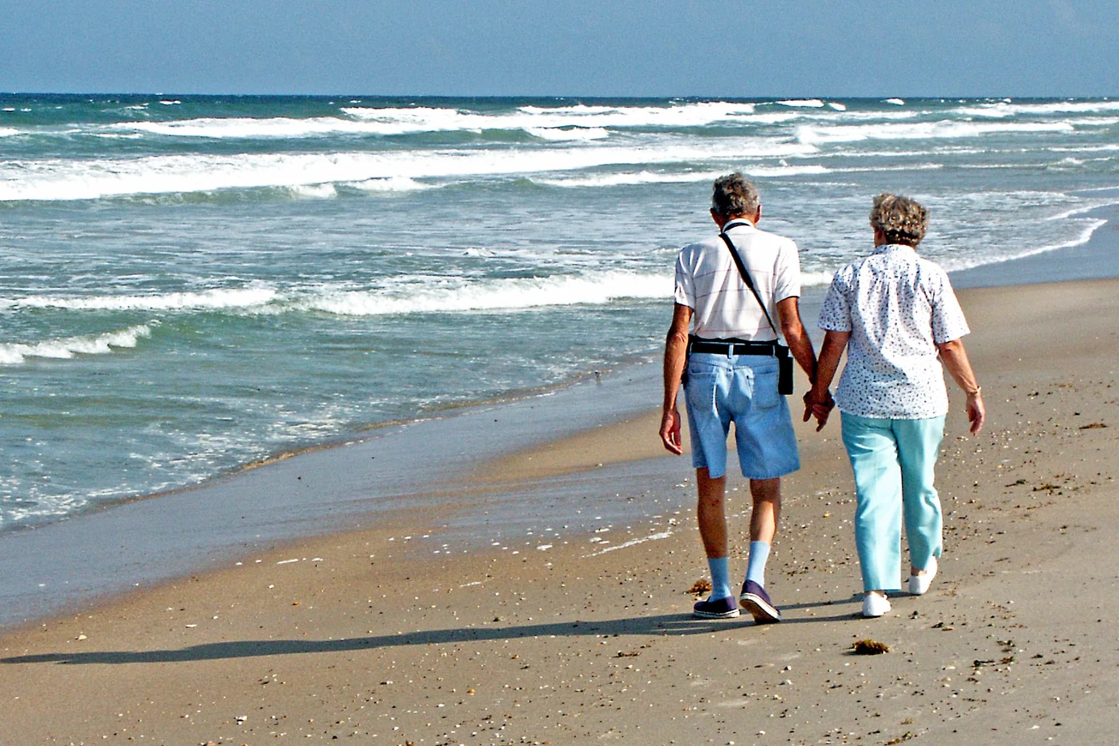 Senior couple walking together along a sunny Florida beach.